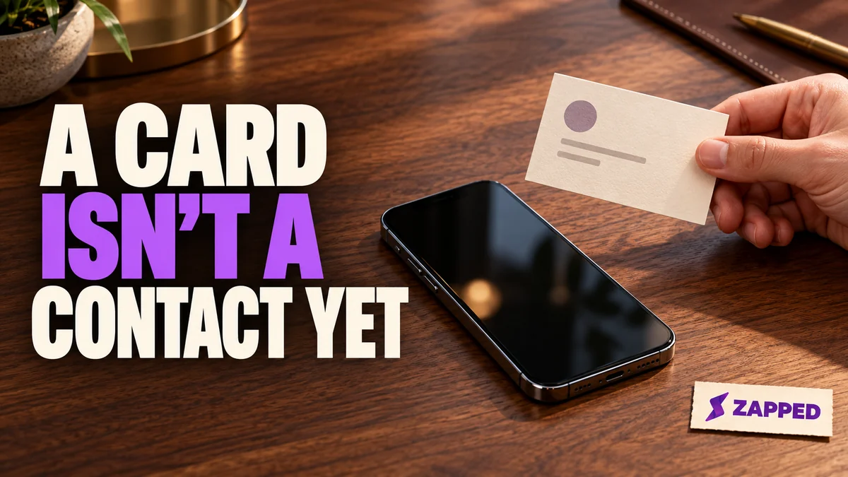 A paper business card held beside an iPhone on a conference table.